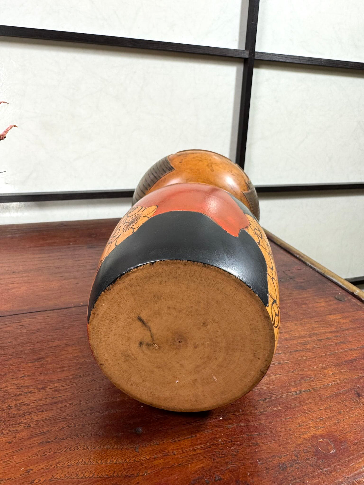 Kokeshi vintage de Yūji Kawase datée de 1977, en bois, à fleurs pyrogravées, grands aplats noirs et rouge brique en puzzle et visage aux yeux clos, le dessous