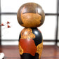 Kokeshi vintage de Yūji Kawase datée de 1977, en bois, à fleurs pyrogravées, grands aplats noirs et rouge brique en puzzle et visage aux yeux clos, 25 cm.