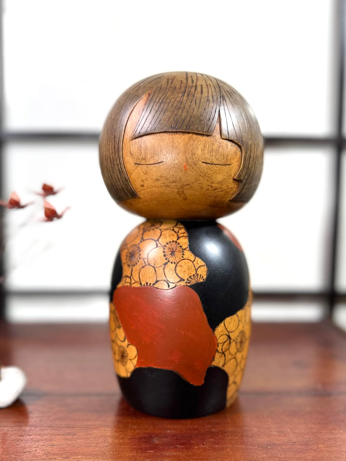 Kokeshi vintage de Yūji Kawase datée de 1977, en bois, à fleurs pyrogravées, grands aplats noirs et rouge brique en puzzle et visage aux yeux clos, 25 cm.