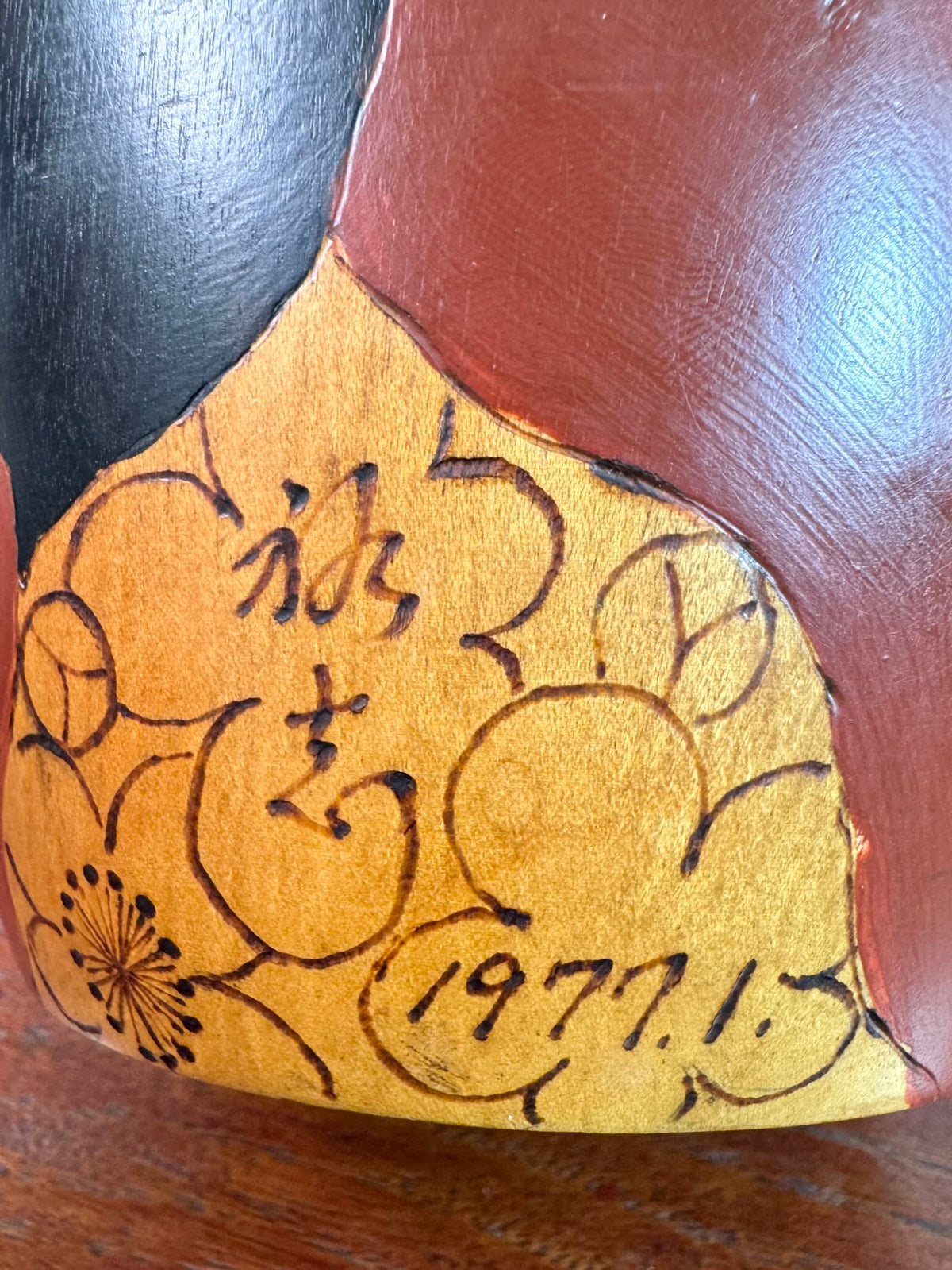 Kokeshi vintage de Yūji Kawase datée de 1977, en bois, à fleurs pyrogravées, grands aplats noirs et rouge brique en puzzle et visage aux yeux clos, la signature et la date pyrogravées