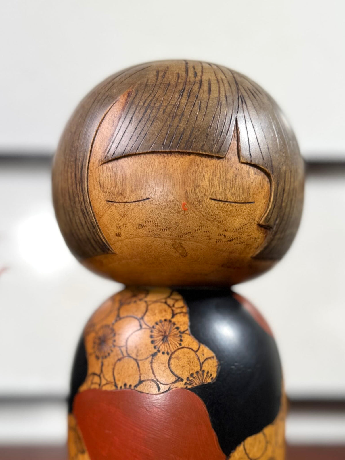 Kokeshi vintage de Yūji Kawase datée de 1977, en bois, à fleurs pyrogravées, grands aplats noirs et rouge brique en puzzle et visage aux yeux clos, gros plan sur le visage