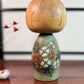 Kokeshi Yuji Kawase de 1979 à décor floral vert, rouge et blanc.
