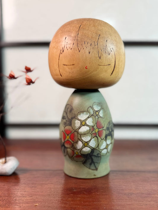Kokeshi Yuji Kawase de 1979 à décor floral vert, rouge et blanc.