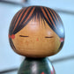 Kokeshi Yuji Kawase verte avec feuilles de vigne d’automne, gros plan sur le visage entouré de couettes