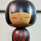 Kokeshi Yuji Kawase noire décorée de grandes fleurs rouges, gros plan sur le visage souriant