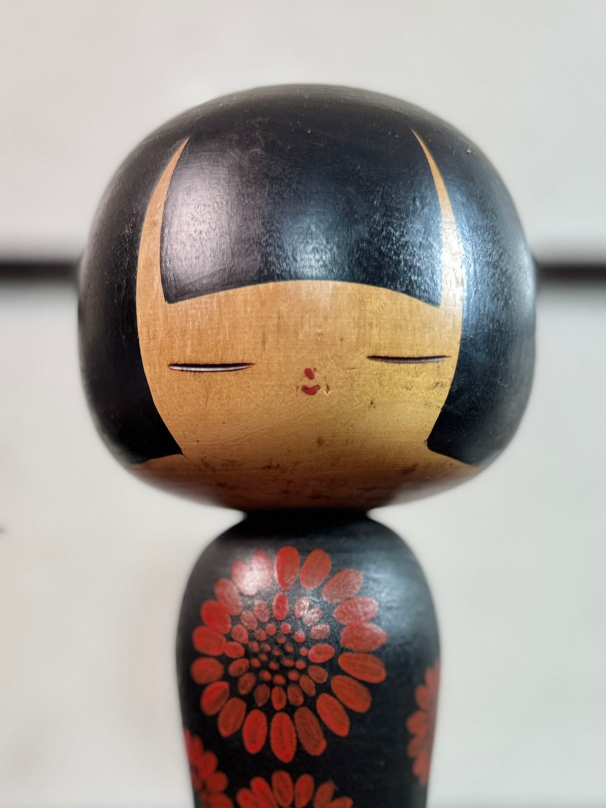 Kokeshi Yuji Kawase noire décorée de grandes fleurs rouges, gros plan sur le visage souriant