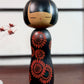 Kokeshi Yuji Kawase noire décorée de grandes fleurs rouges.