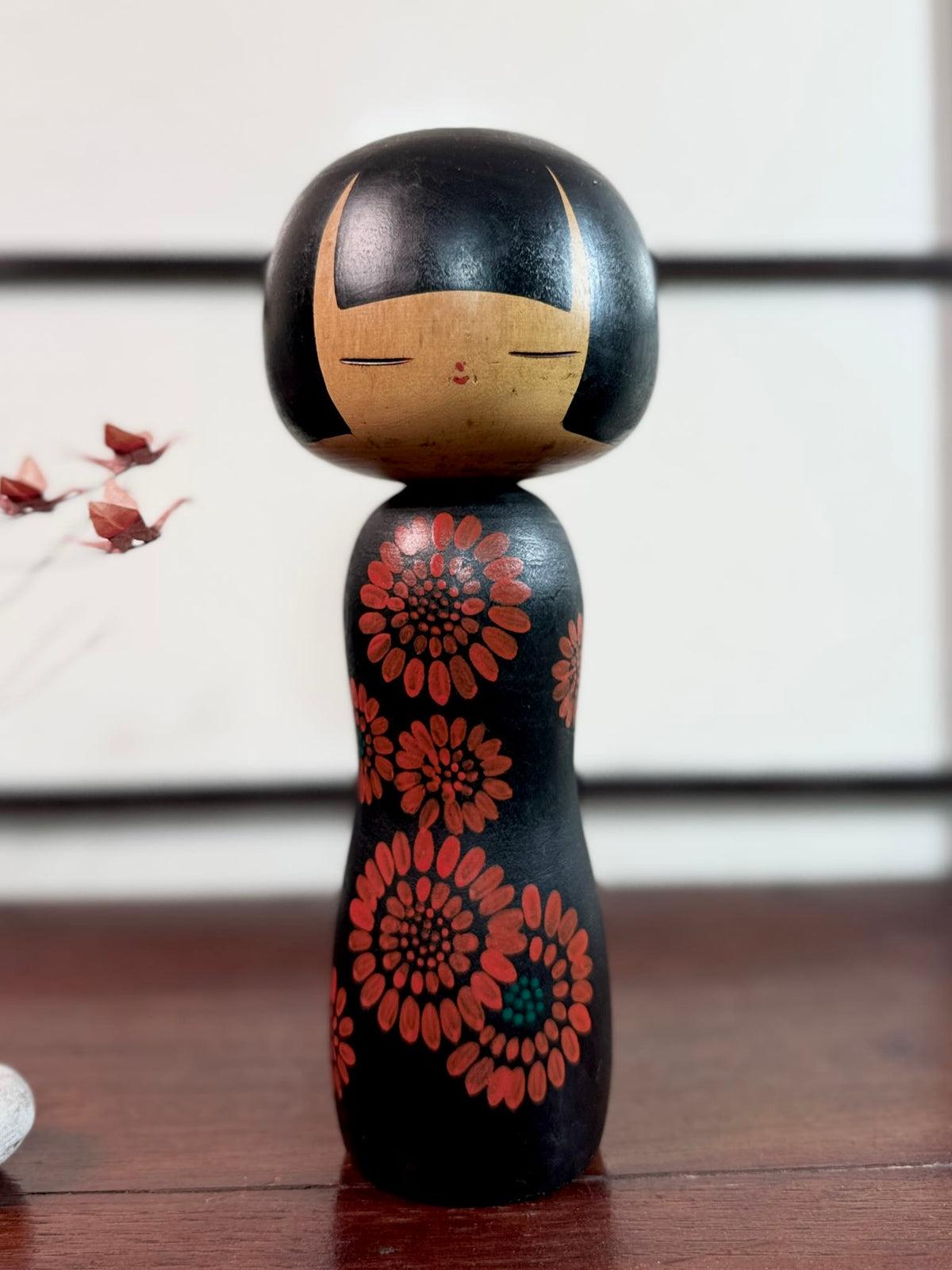 Kokeshi Yuji Kawase noire décorée de grandes fleurs rouges.
