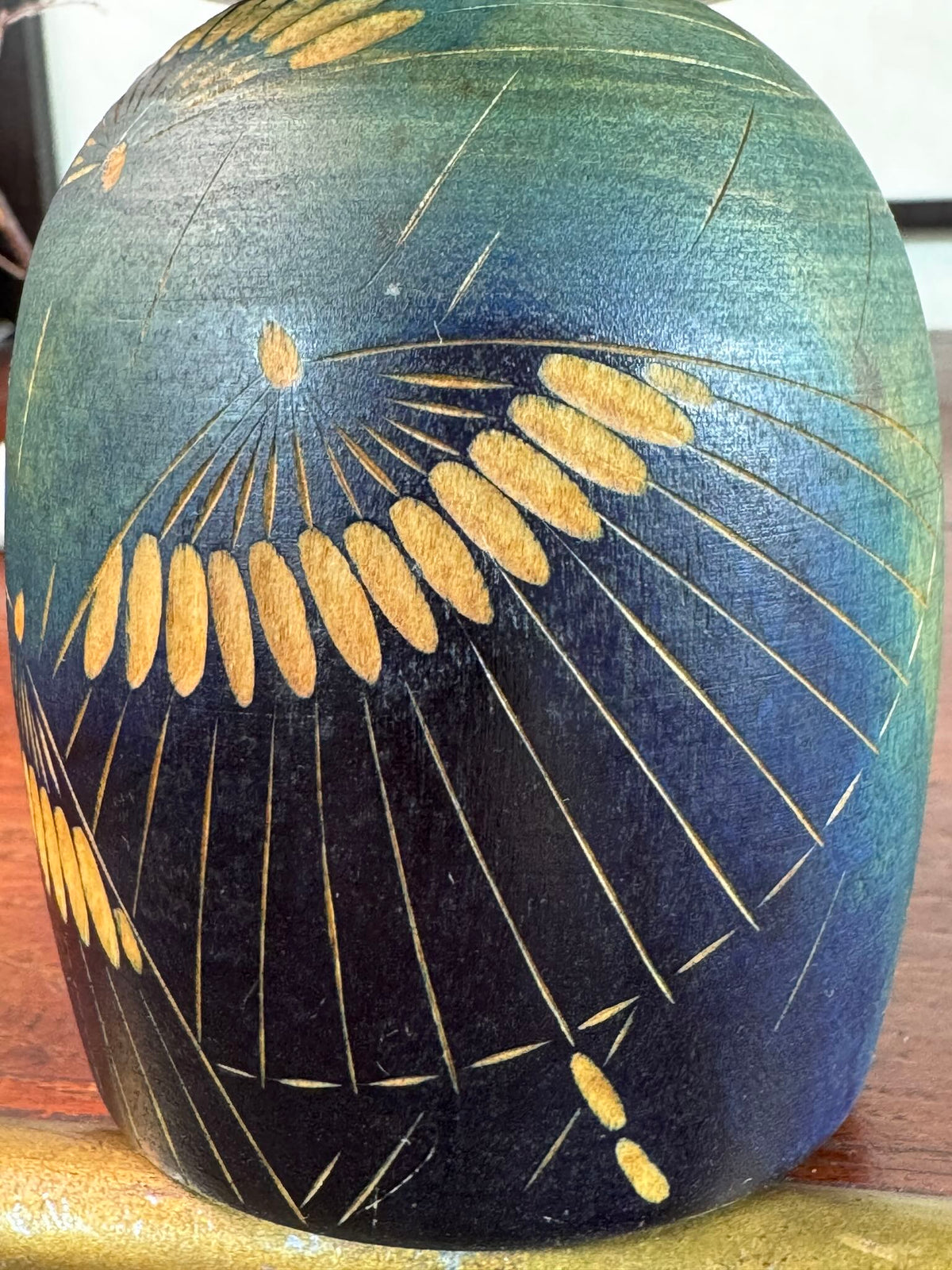 Kokeshi Yuji Kawase bleu-vert avec parapluies gravés et chignon, gros p^lan sur le corps bleu gravé.