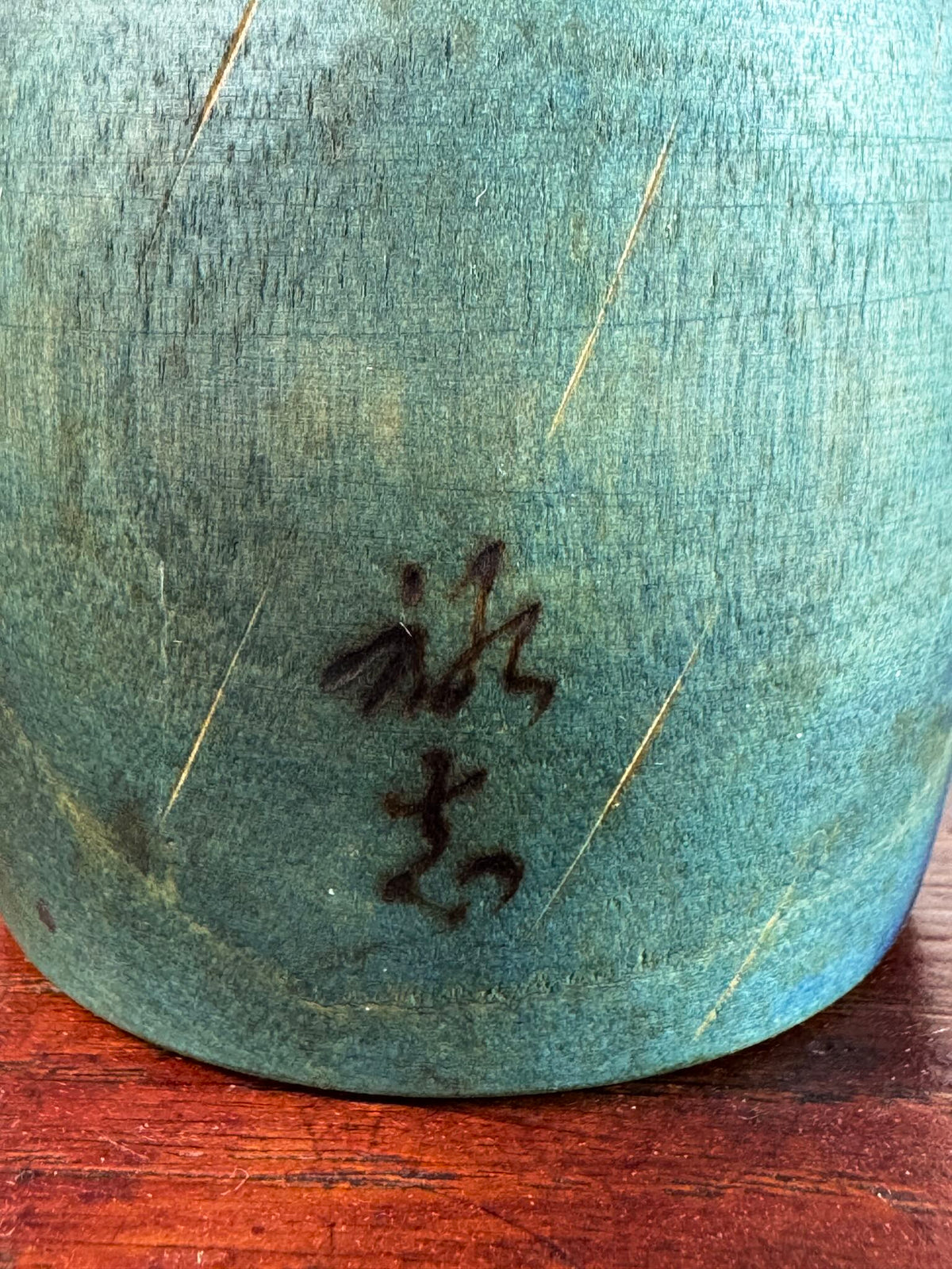 Kokeshi Yuji Kawase bleu-vert avec parapluies gravés et chignon, gros plan sur la signature.
