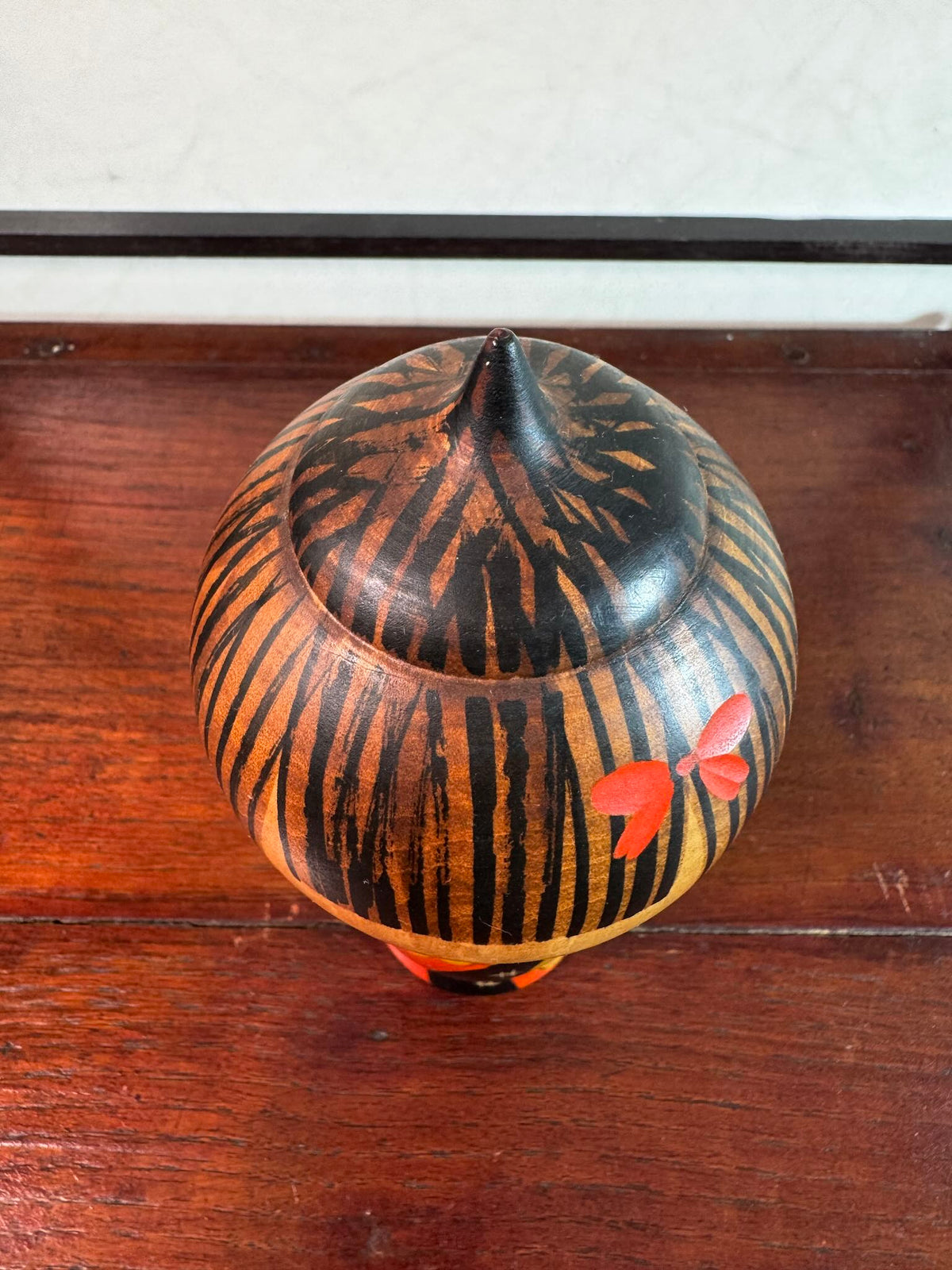 Kokeshi Yuji Kawase au kimono rouge fleuri et coiffure pointue, gros plan sur le dessus de la tête