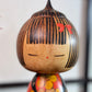 Kokeshi Yuji Kawase au kimono rouge fleuri et coiffure pointue, gros plan sur la tête