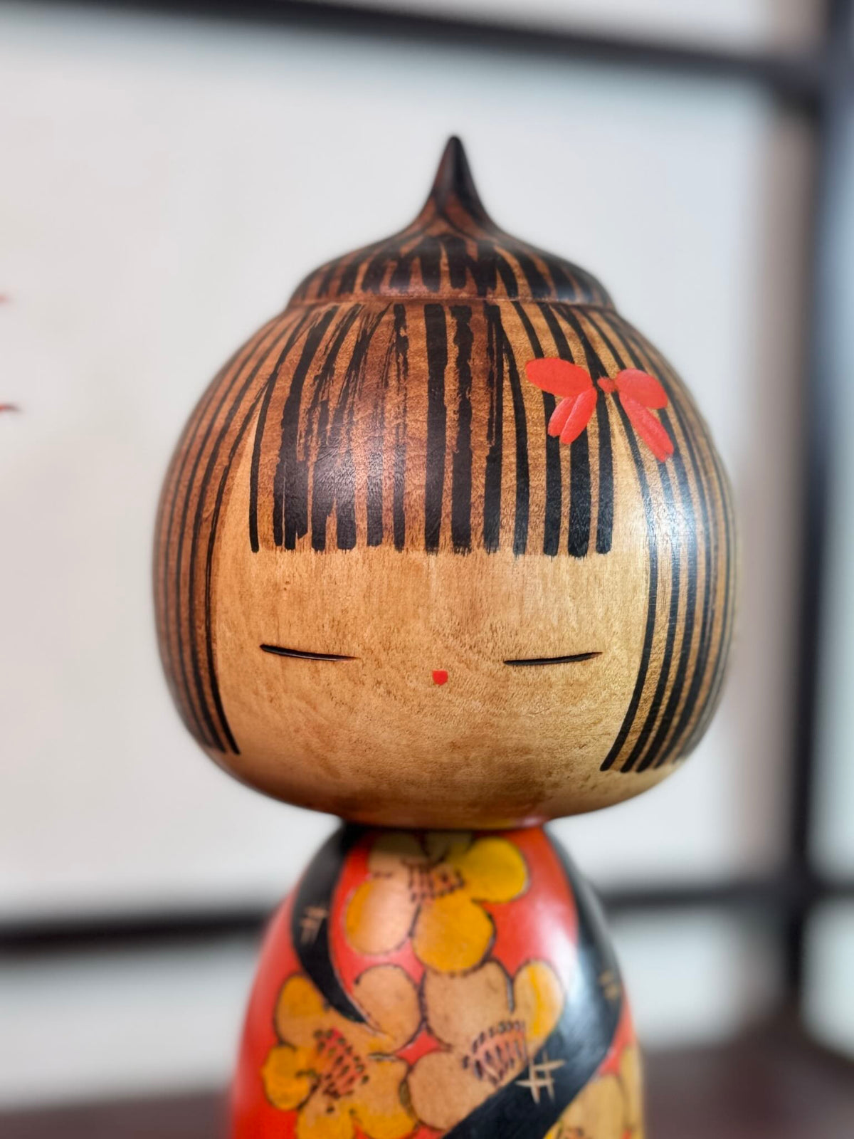 Kokeshi Yuji Kawase au kimono rouge fleuri et coiffure pointue, gros plan sur la tête