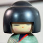 Kokeshi Yuji Kawase Asanoha au kimono vert et bleu gros plan sur le visage souriant