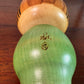 Kokeshi Yuji Kawase au kimono vert fleuri et coiffure à boules, la signature au dos
