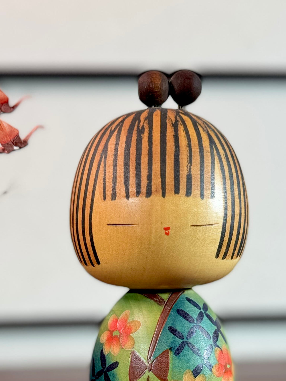 Kokeshi Yuji Kawase au kimono vert fleuri et coiffure à boules, gros plan sur le visage