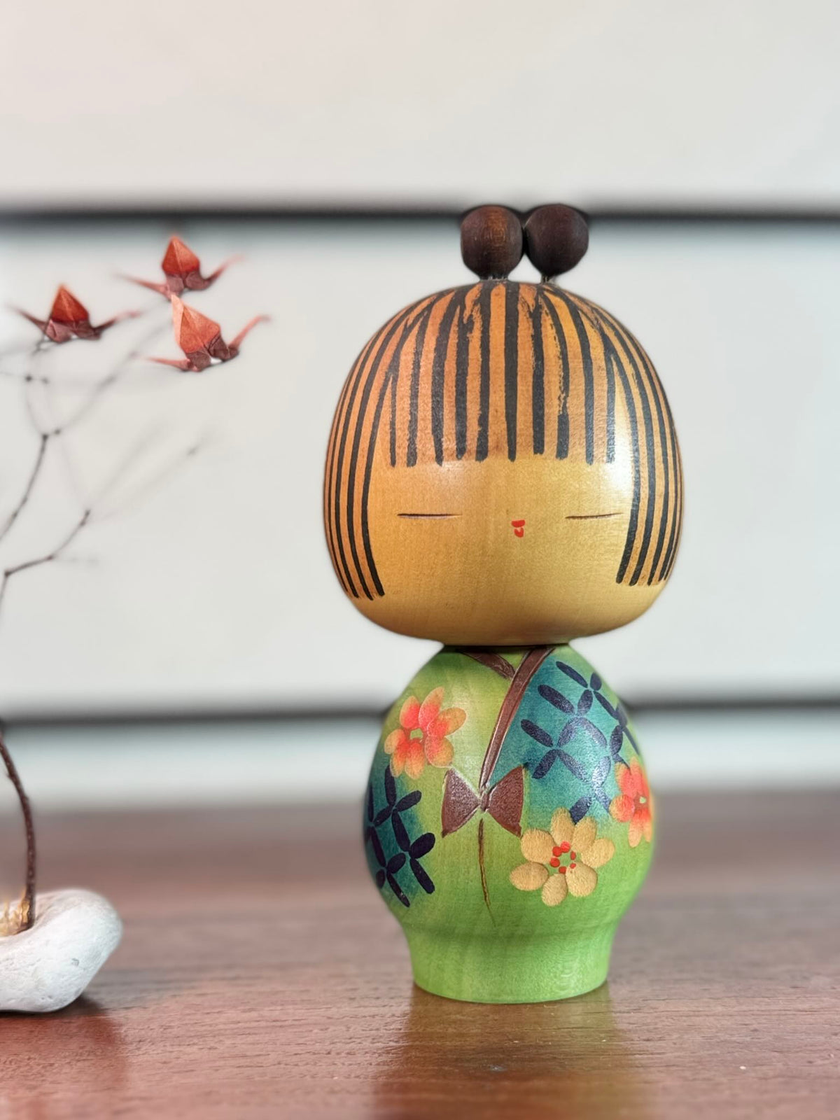 Kokeshi Yuji Kawase au kimono vert fleuri et coiffure à boules.