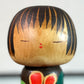 Kokeshi Yuji Kawase brune aux fleurs rouges et roses, gros plan sur le visage