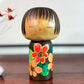 Kokeshi Yuji Kawase brune aux fleurs rouges et roses.