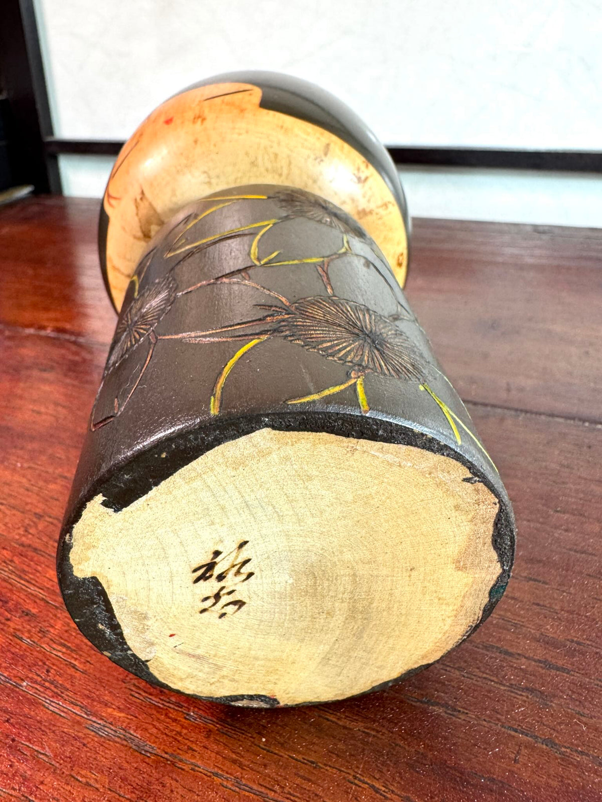 Kokeshi vintage de Yuji Kawase caractérisée par une grande tête brune, un corps étroit et un décor de fleurs gravées, la signature de l'artisan au dessous