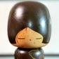 Kokeshi vintage de Yuji Kawase caractérisée par une grande tête brune, un corps étroit et un décor de fleurs gravées, gros plan sur le visage souriant