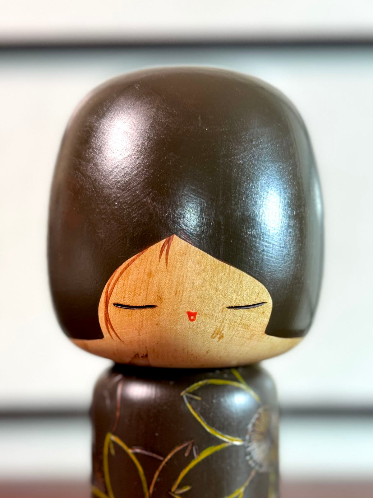 Kokeshi vintage de Yuji Kawase caractérisée par une grande tête brune, un corps étroit et un décor de fleurs gravées, gros plan sur le visage souriant