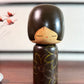 Kokeshi vintage de Yuji Kawase caractérisée par une grande tête brune, un corps étroit et un décor de fleurs gravées.