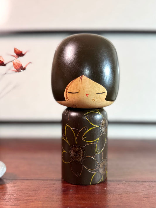 Kokeshi vintage de Yuji Kawase caractérisée par une grande tête brune, un corps étroit et un décor de fleurs gravées.