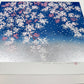 estampe japonaise contemporaine de Namiki Hajime cerisier en fleurs et pétales volant sur ciel bleu et argent, vu de 3/4