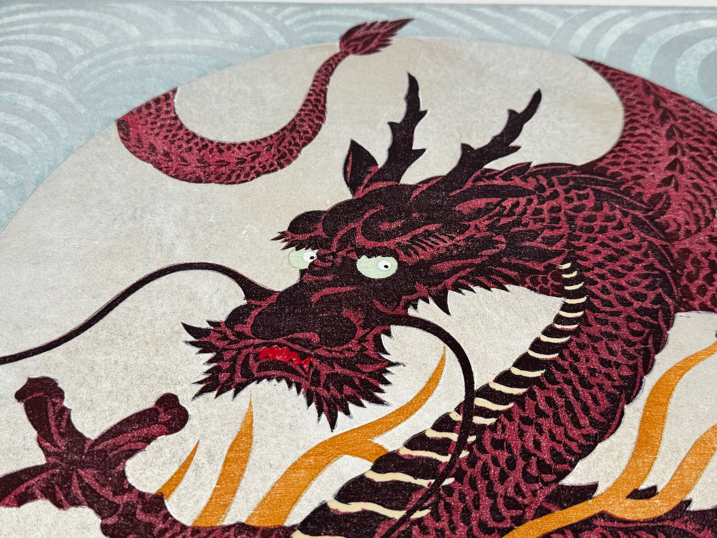estampe japonaise dragon rouge sur fond argent à volutes, la tête du dragon gueule fermée