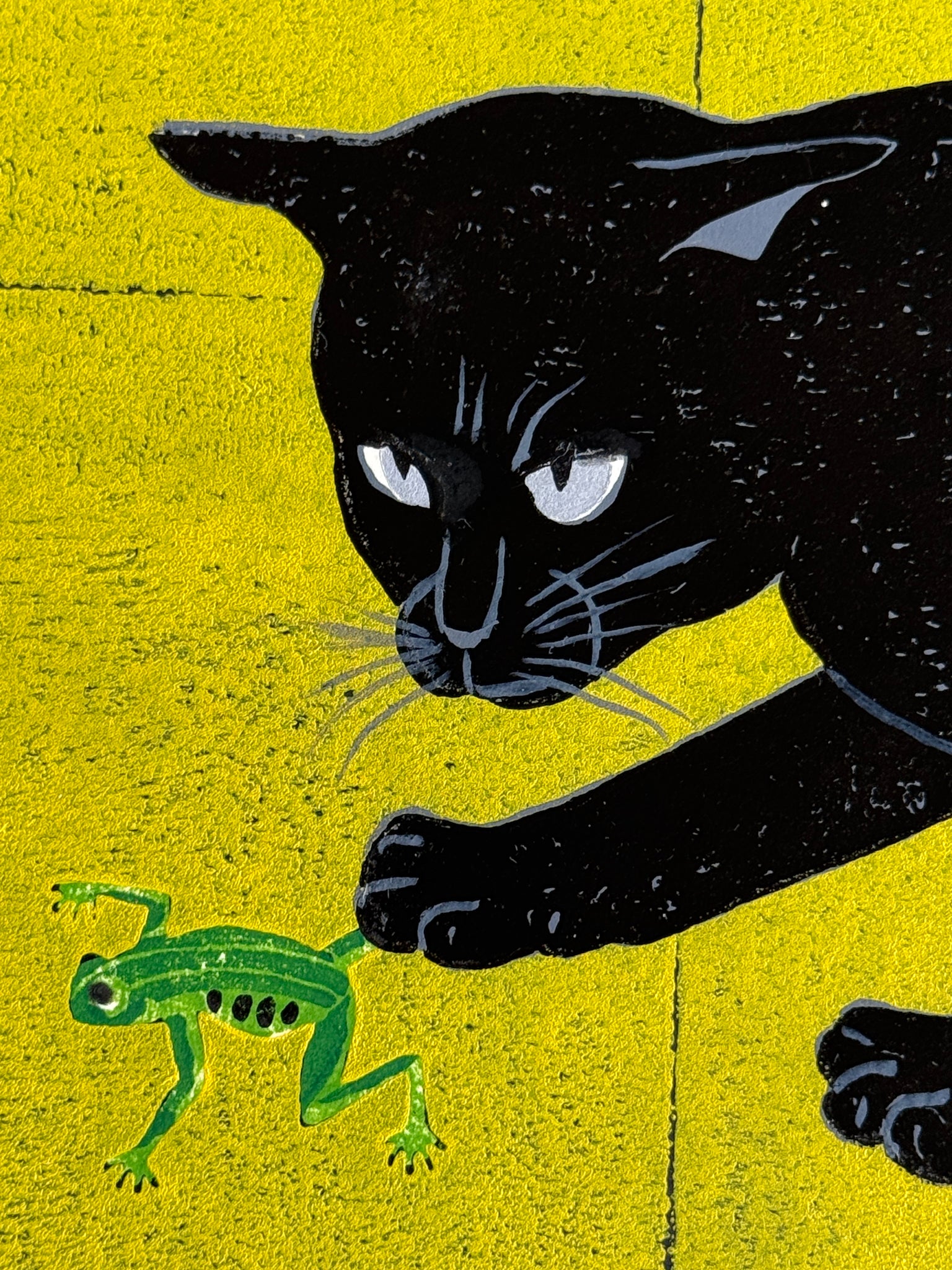 Estampe japonaise de Nishida montrant un chat noir jouant avec une grenouille sur fond vert et jaune, gros plan sur la tête