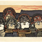 estampe japonaise de Nishijima, un groupe de tanuki devant des jarres en terre, toit des maisons et ciel jaune orange en arrière plan