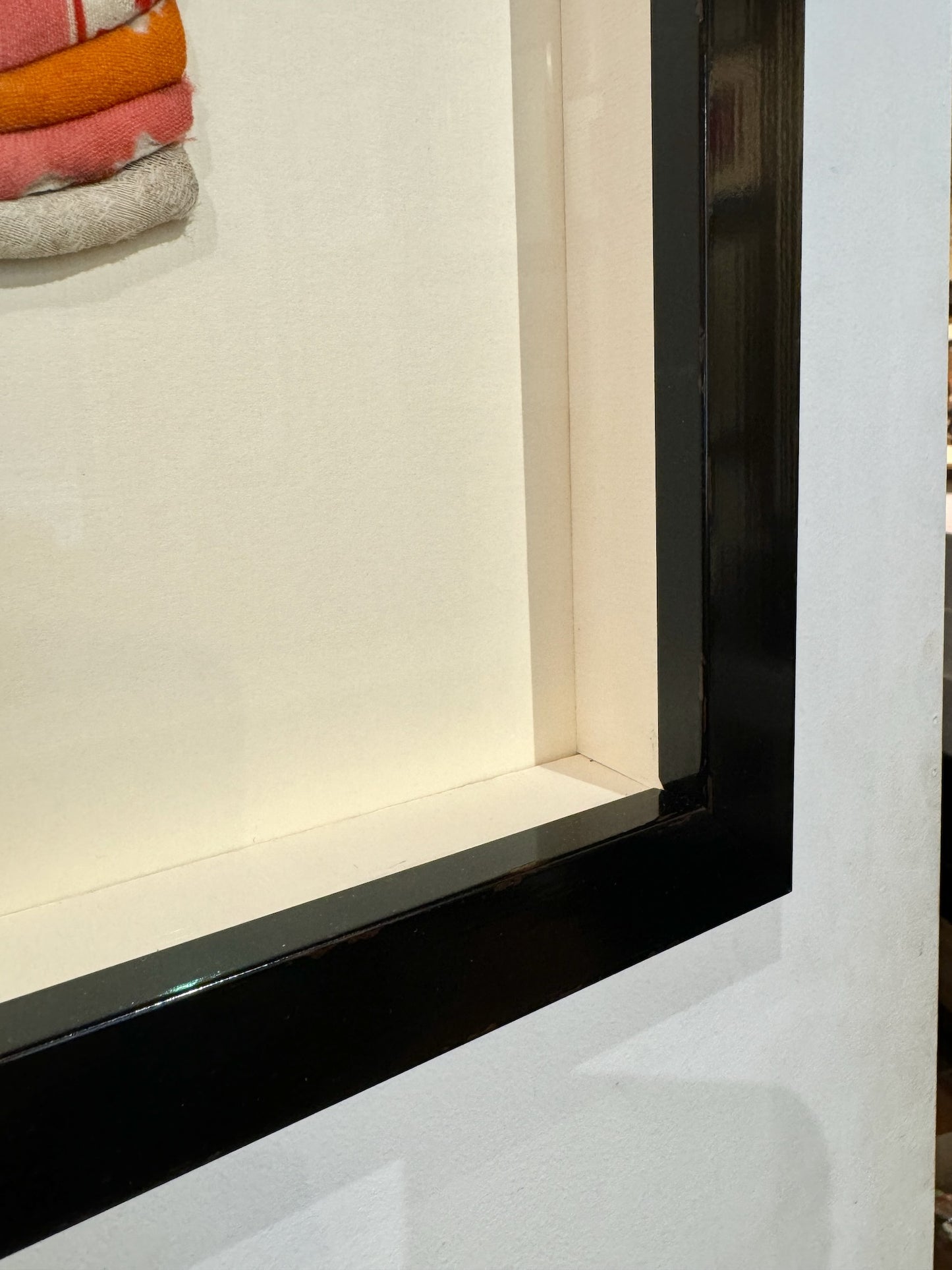 Okiyage japonais encadré représentant une femme en kimono à plusieurs couches de tissu coloré, monté en relief et présenté dans un cadre vitré noir, gros plan sur l'angle du cadre noir laqué