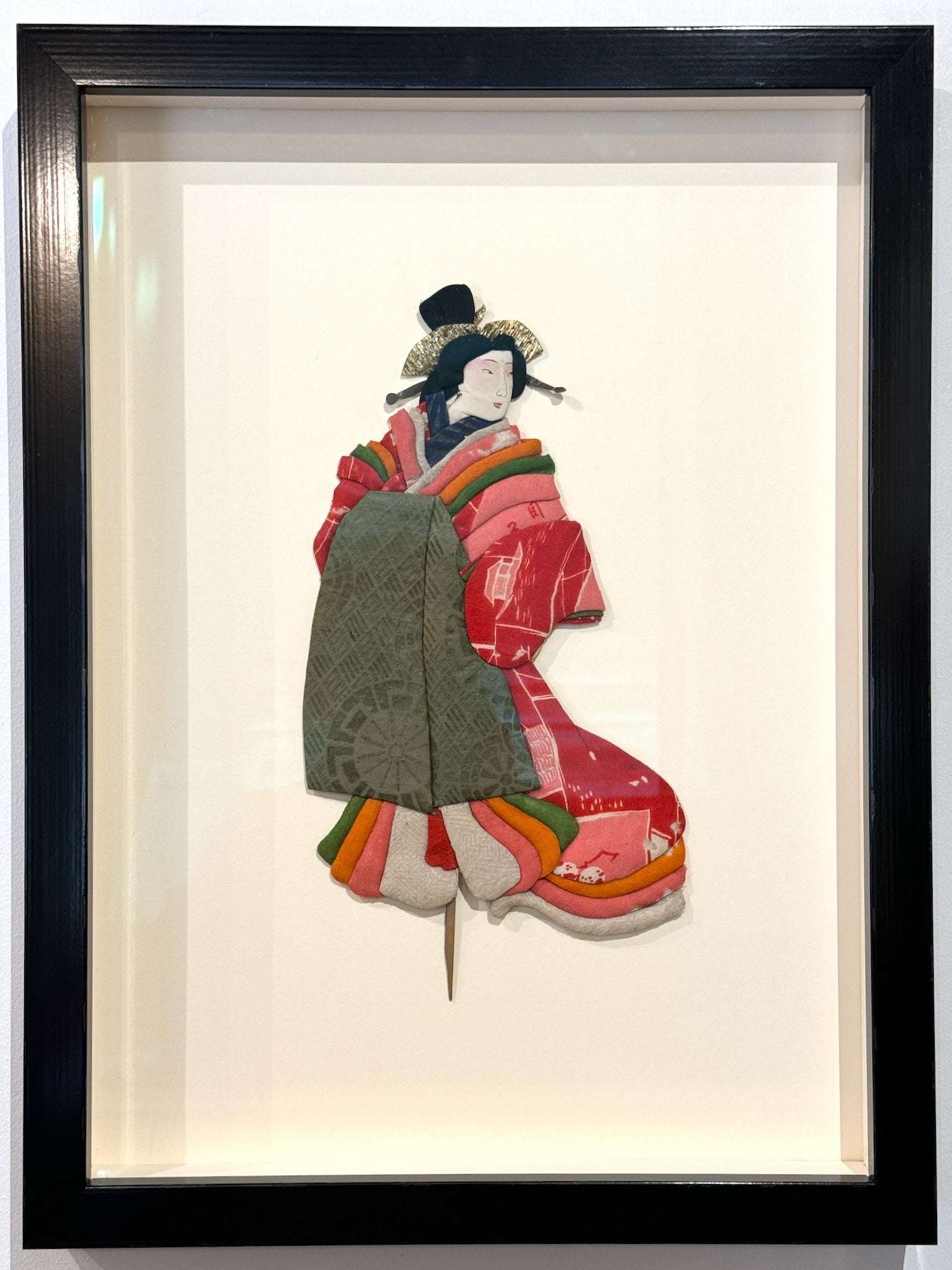 Okiyage japonais encadré représentant une femme en kimono à plusieurs couches de tissu coloré, monté en relief et présenté dans un cadre vitré noir.