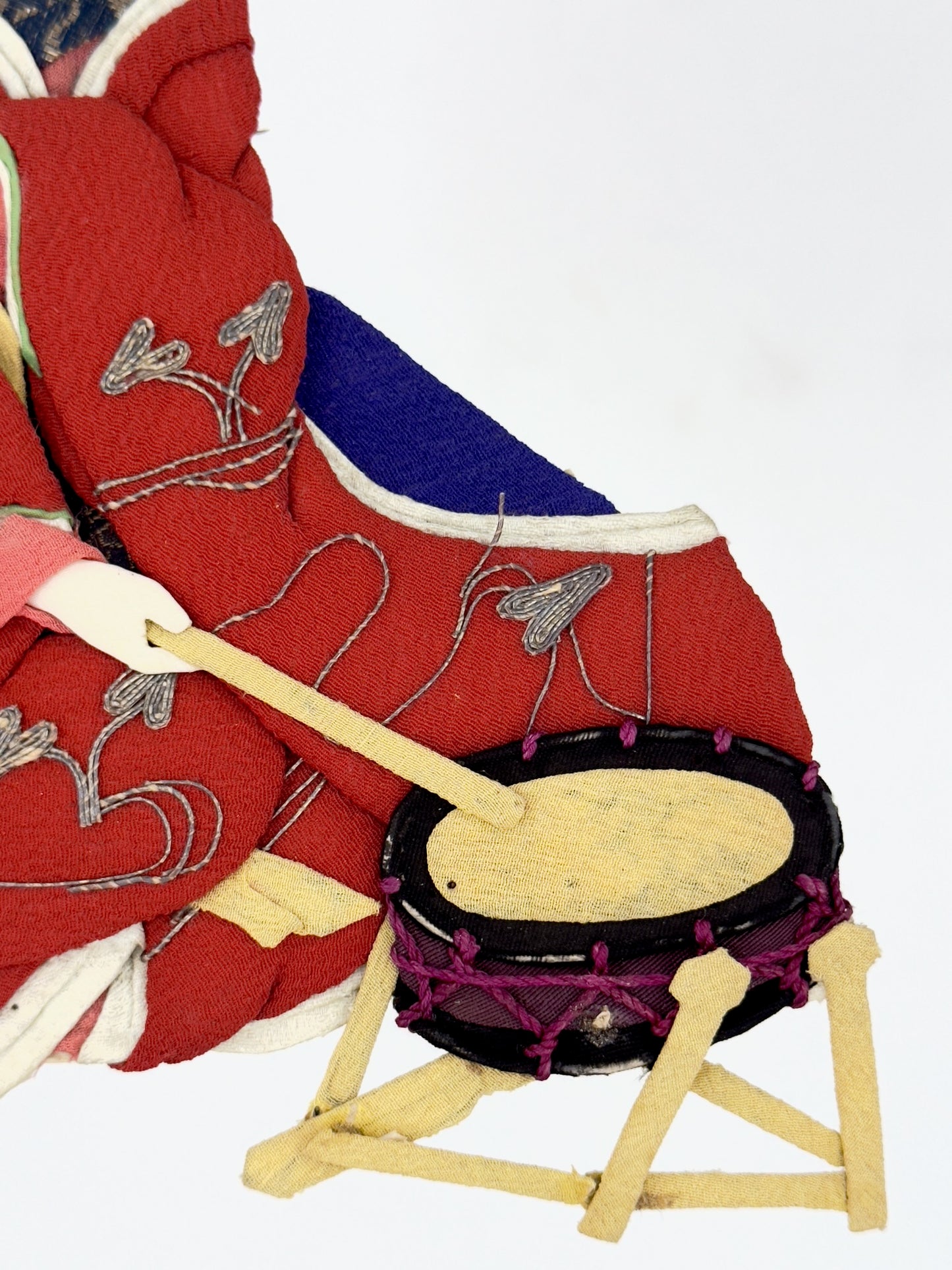 Okiyage japonais représentant une femme jouant du tambour, vêtue d’un kimono rouge brodé, coiffée de fleurs et rubans, réalisée en tissu, gros plan sur le tambour