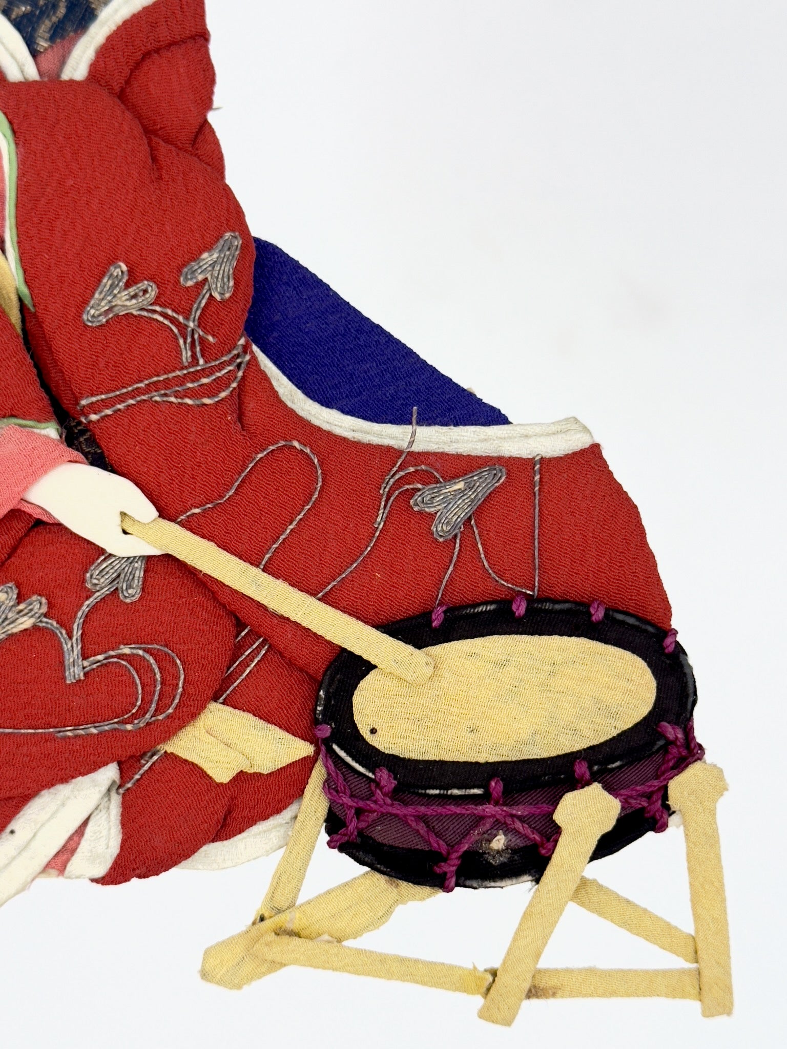 Okiyage japonais représentant une femme jouant du tambour, vêtue d’un kimono rouge brodé, coiffée de fleurs et rubans, réalisée en tissu, gros plan sur le tambour