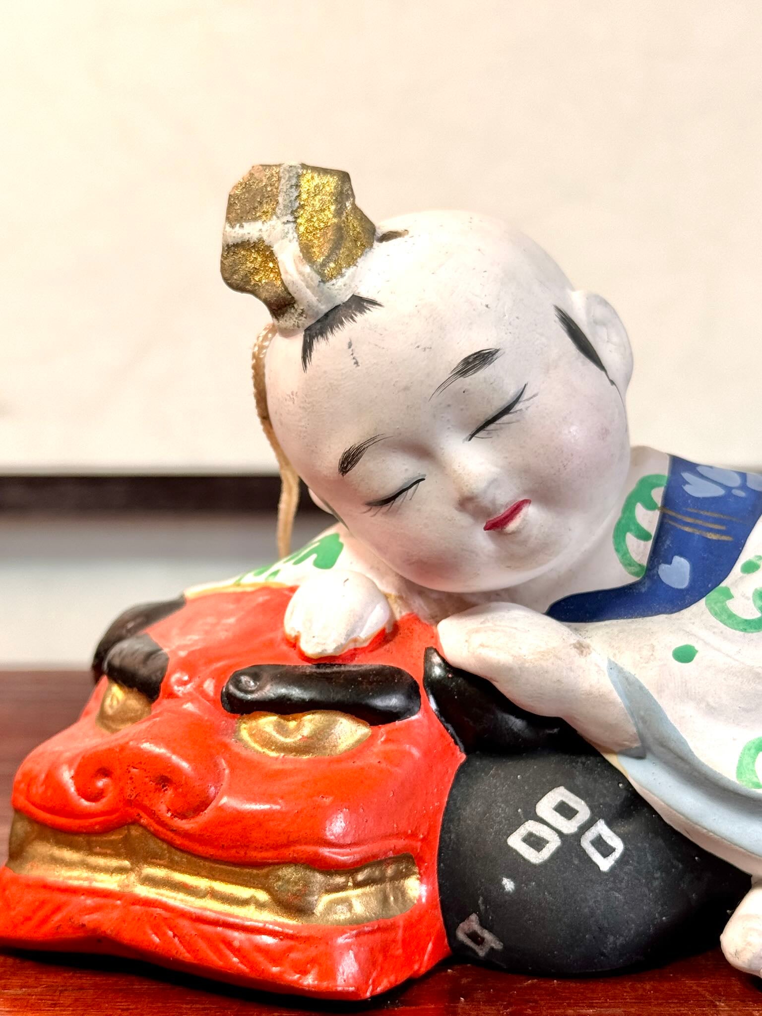 céramique japonaise,enfant endormi sur tete de lion shishi, gros plan sur le visage de l'enfant et la tête de lion rouge aux yeux dorés