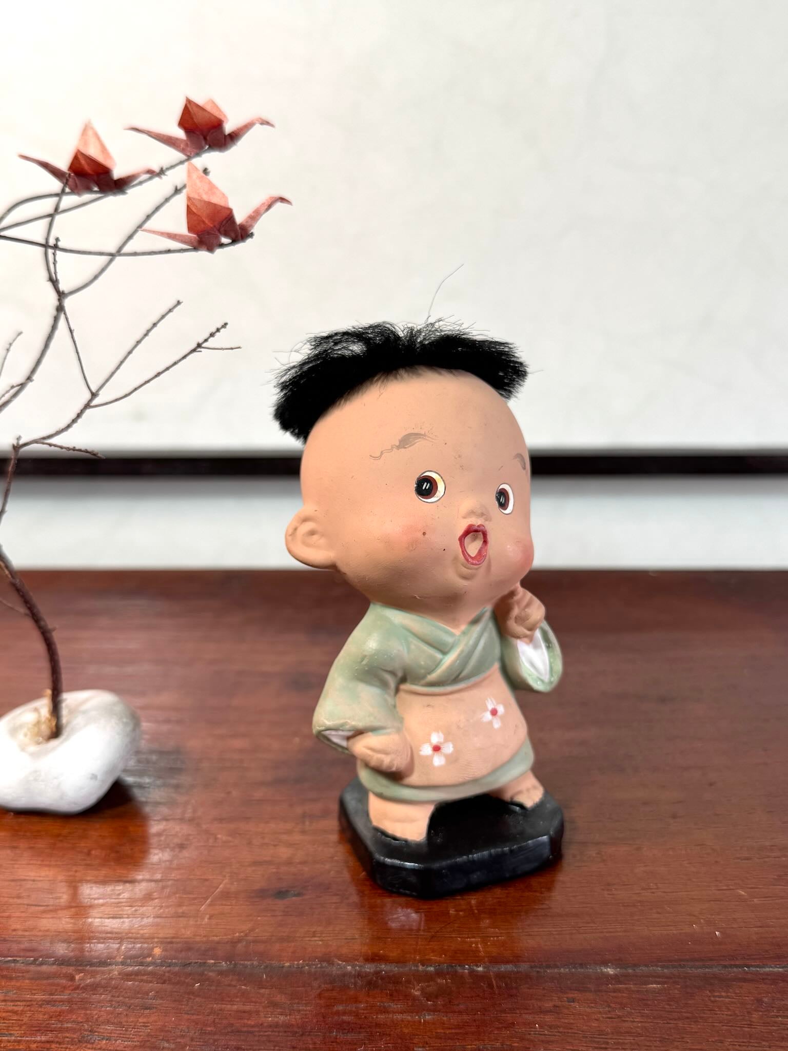 Figurine japonaise ancienne d’enfant étonné en céramique avec cheveux noirs, vu de 3/4