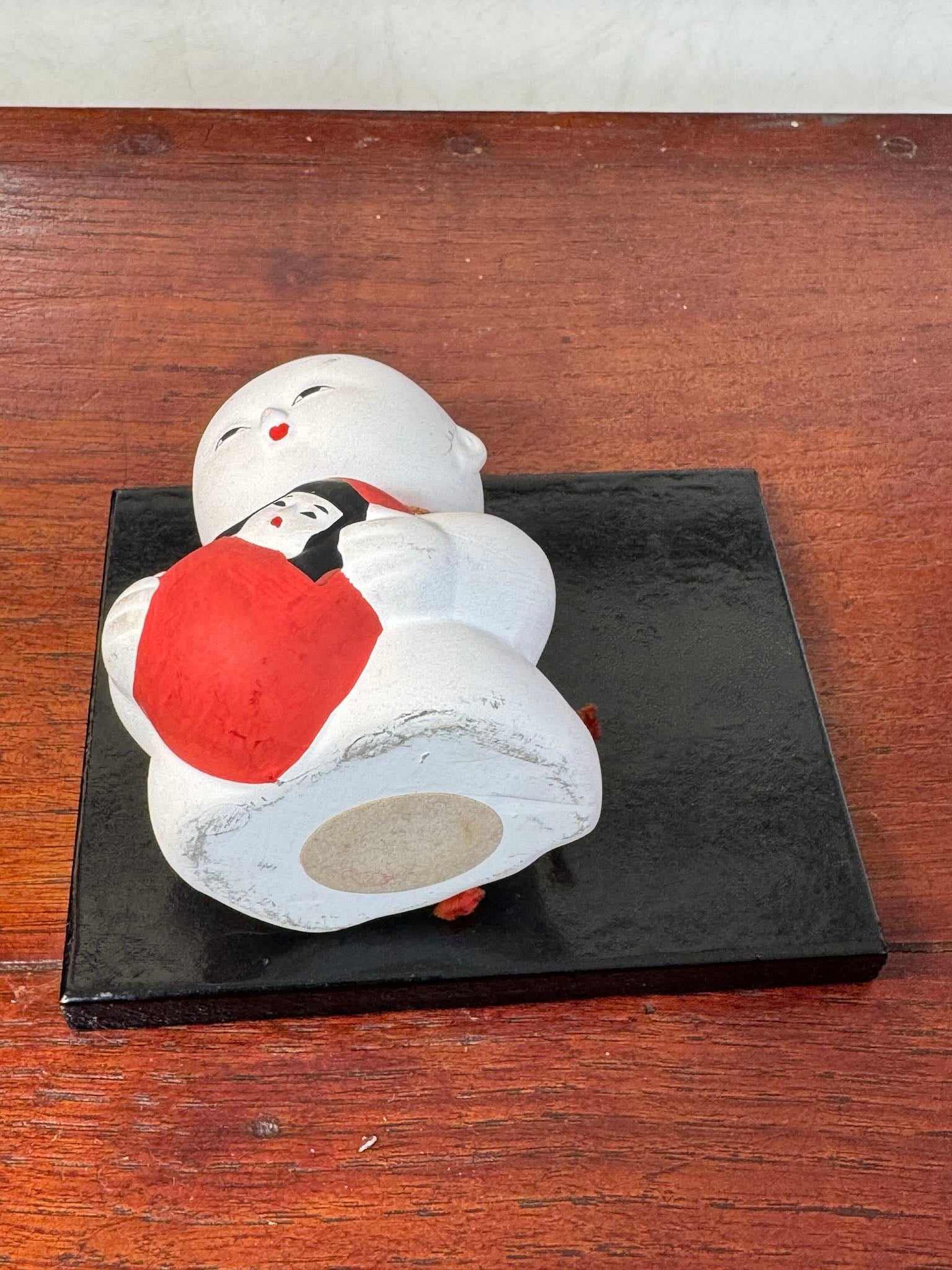 Gosho Ningyō en céramique tenant un Hime Daruma rouge japonais, vu de dessous