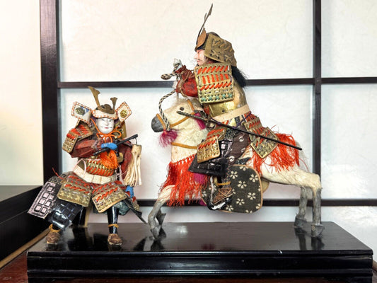 poupées japonaises sur socle laqué représentant un samouraï dans deux attitudes différentes, en action sur un cheval blanc et assis en réflexion