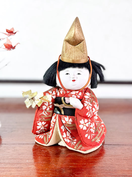 Poupée japonaise Kimekomi en kimono rouge avec chapeau doré et bâton rituel shintō, vu de face.