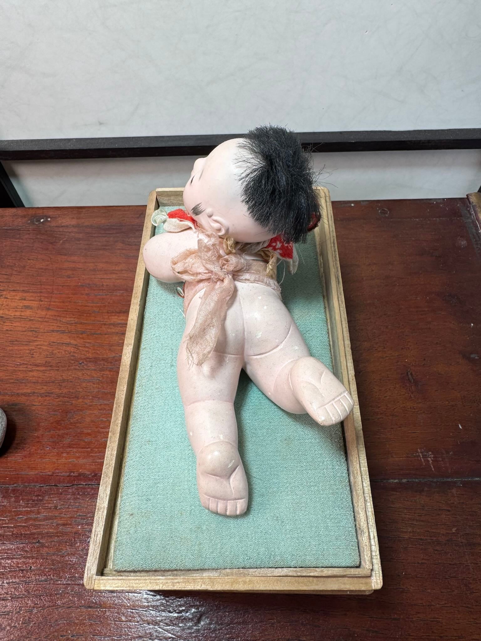 Poupée japonaise ancienne bébé couché en terre cuite sur boite en bois, vu de dessus