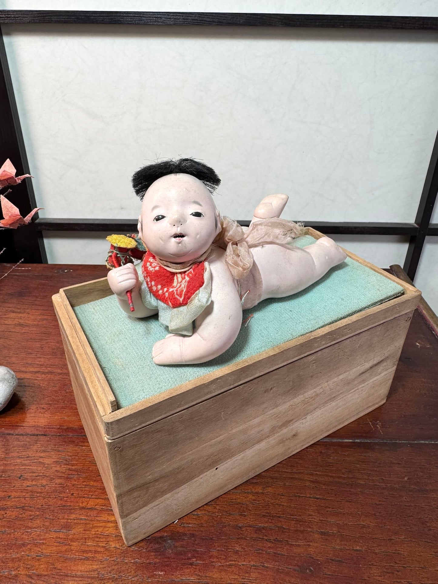 Poupée japonaise ancienne bébé couché en terre cuite sur boite en bois, vu de 3/4