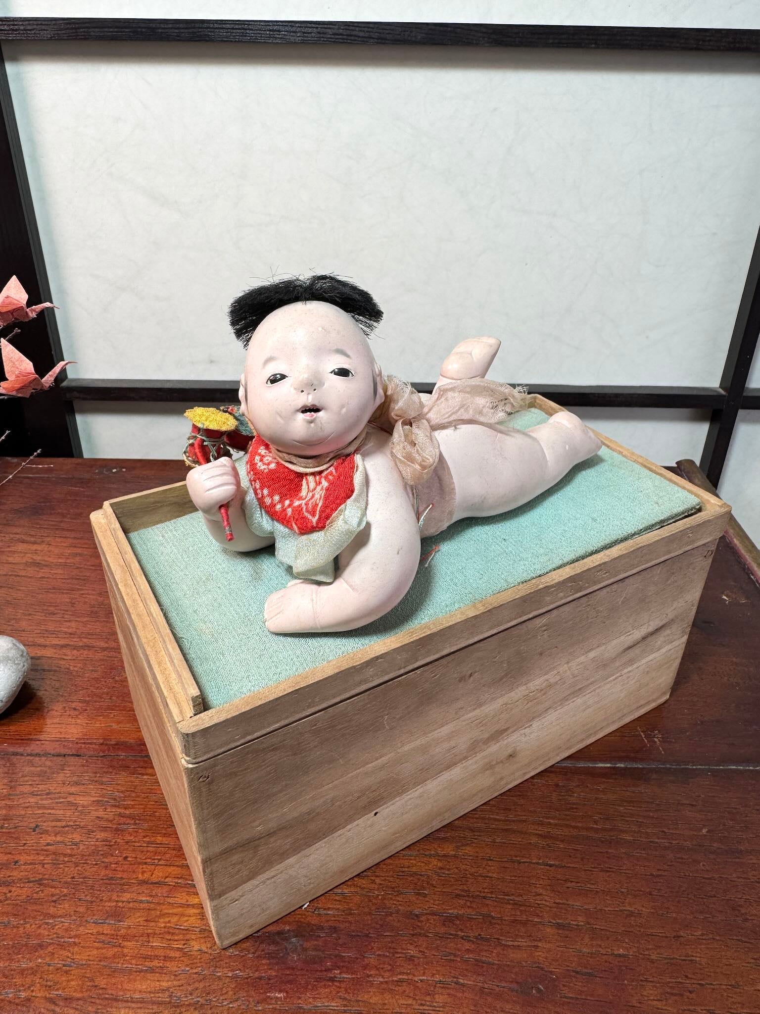 Poupée japonaise ancienne bébé couché en terre cuite sur boite en bois, vu de 3/4