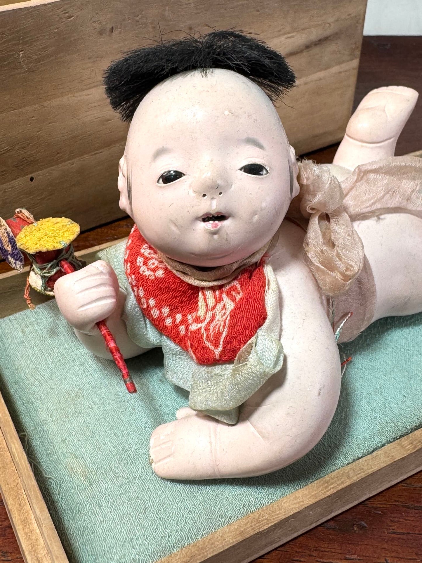 Poupée japonaise ancienne bébé couché en terre cuite sur boite en bois, gros plan sur le visage avec yeux incrusté en pate de verre