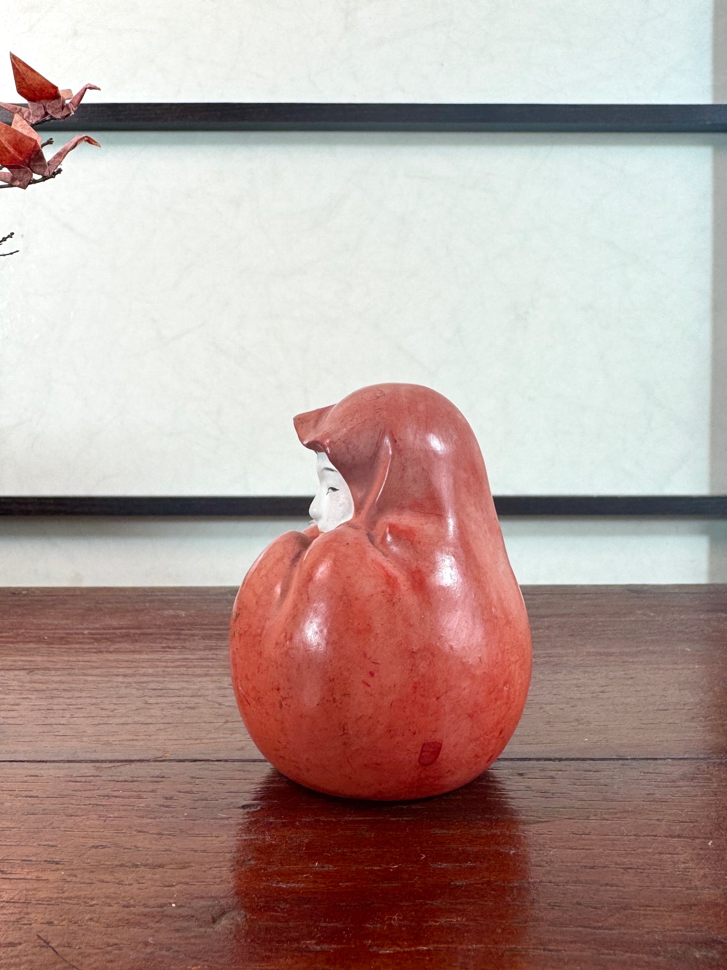 Statuette japonaise en céramique rouge représentant une princesse Daruma au visage délicat, vu du profil gauche