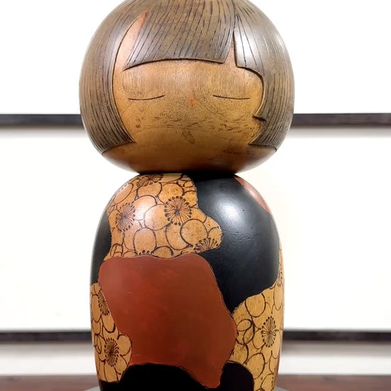 Kokeshi vintage de Yūji Kawase datée de 1977, en bois, à fleurs pyrogravées, grands aplats noirs et rouge brique en puzzle et visage aux yeux clos, la vidéo à 360 degrés