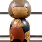 Kokeshi vintage de Yūji Kawase datée de 1977, en bois, à fleurs pyrogravées, grands aplats noirs et rouge brique en puzzle et visage aux yeux clos, la vidéo à 360 degrés