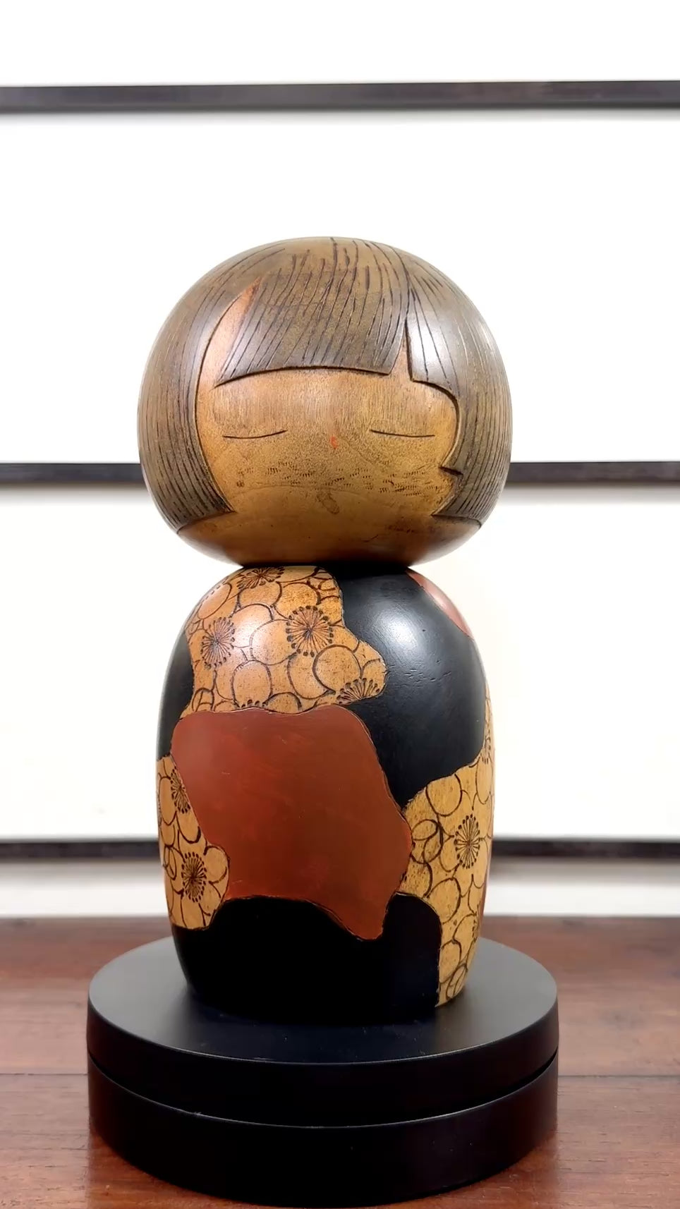 Kokeshi vintage de Yūji Kawase datée de 1977, en bois, à fleurs pyrogravées, grands aplats noirs et rouge brique en puzzle et visage aux yeux clos, la vidéo à 360 degrés