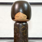 Kokeshi vintage de Yuji Kawase caractérisée par une grande tête brune, un corps étroit et un décor de fleurs gravées, la vidéo à 360 degrés